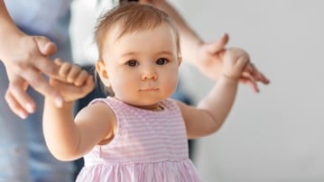 Liten flicka lär sig gå med hjälp av sin mamma.