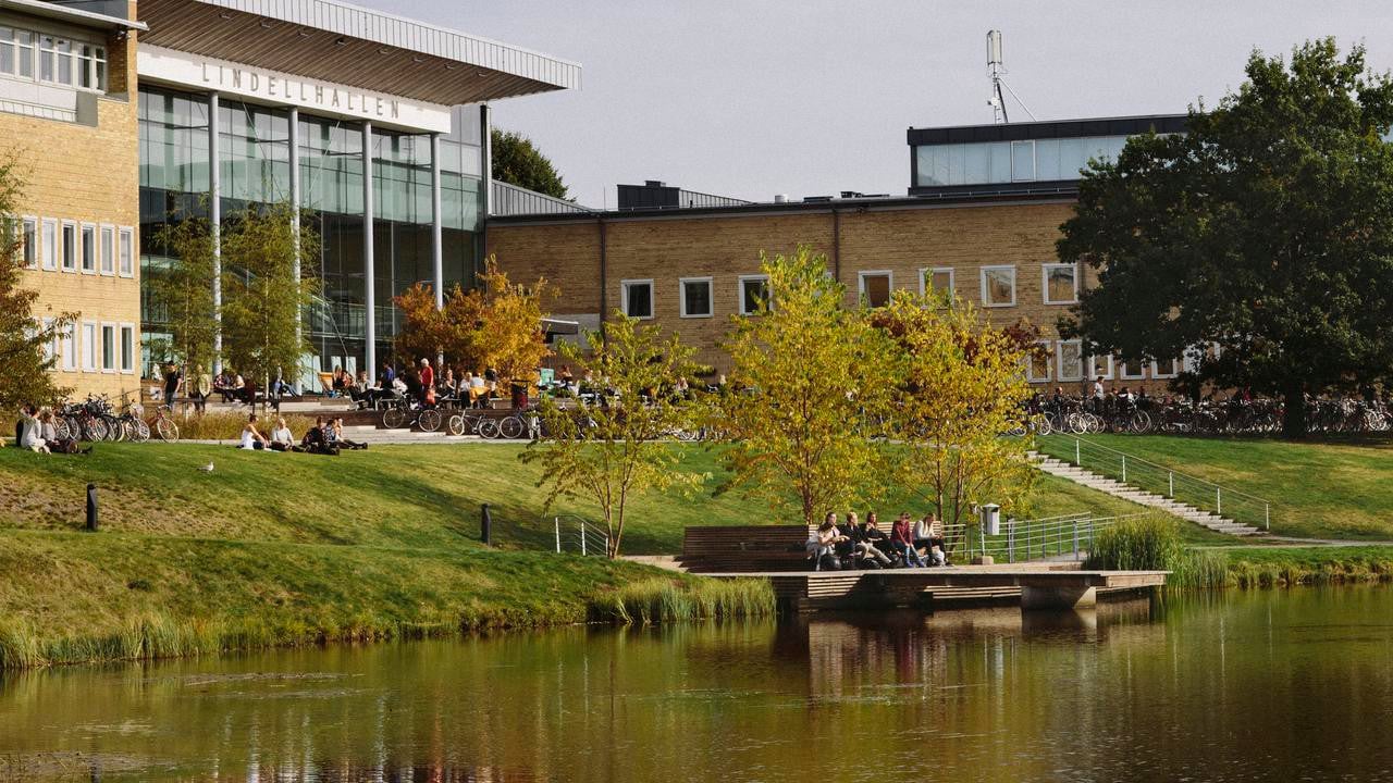Studenter utomhus på campus. Vy över dammen och Lindellhallen. Bilden har formatet 16x9 och är anpassad för att användas som toppbild på studentrekryteringswebben.