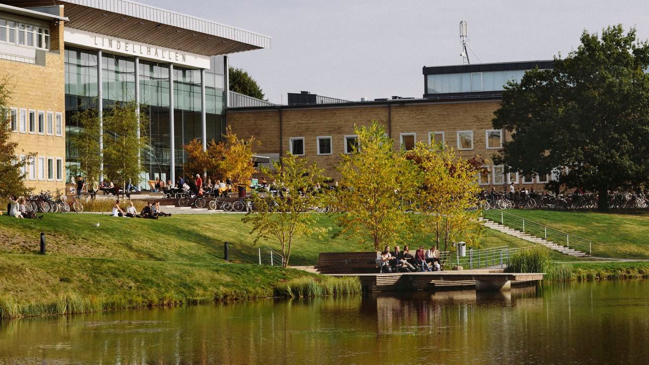 Studenter utomhus på campus. Vy över dammen och Lindellhallen. Bilden har formatet 16x9 och är anpassad för att användas som toppbild på studentrekryteringswebben.