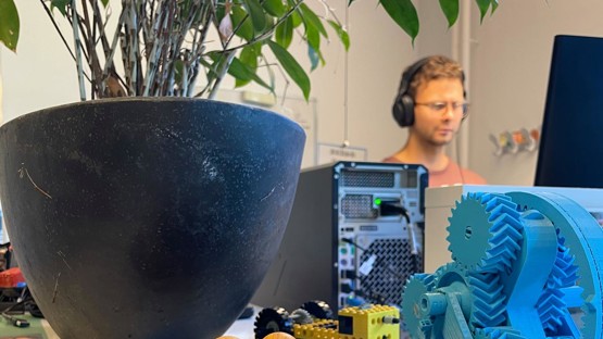 En person som står och jobbar vid sin dator med prylar i framgrunden