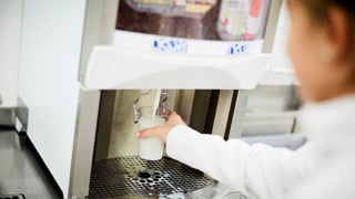 School girl filling glass of milk from machine in school cafeteria