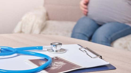 stethoscope and ultrasound scan on the table, pregnant woman sitting on the couch against the background of the doctor's workplace