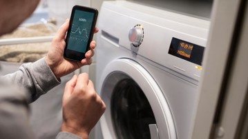 Person tittar på elförbrukning på mobil och tvättmaskin