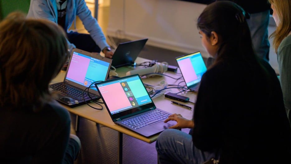 A group of people sitting around a table with laptops.