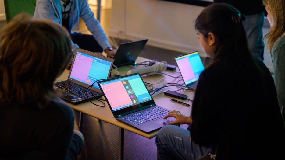 A group of people sitting around a table with laptops.