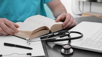 Medical student in uniform studying at table indoors, closeup