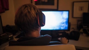 Teenage boy with headphones playing video game in dark bedroom