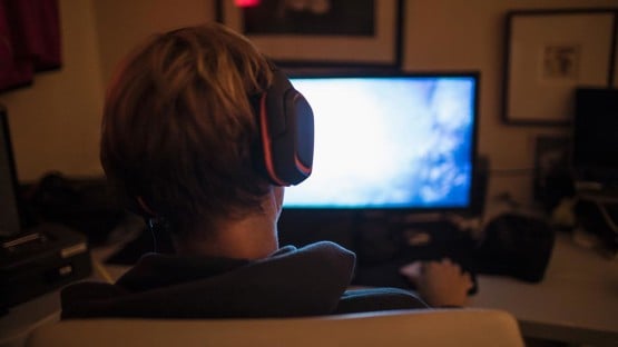 Teenage boy with headphones playing video game in dark bedroom
