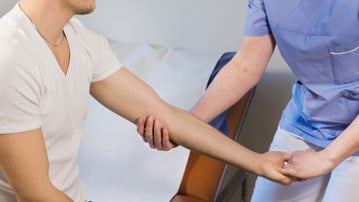 Sjukgymnastsjuksköterska kontrollerar arm på manlig patient