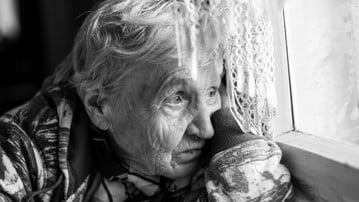Granny older woman sadly looking out the window. Black-and-white photo.