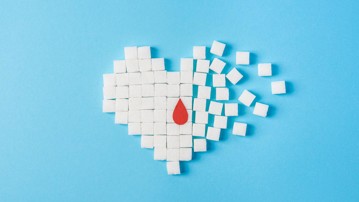the drop of blood on broken heart made of pure white cubes of sugar isolated on blue background, World diabetes day, November 14