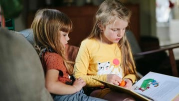 Två barn sitter och läser en barnbok. 