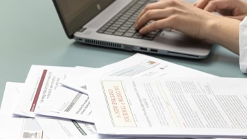 Vetenskapliga artiklar och persons händer som skriver på bärbar dator