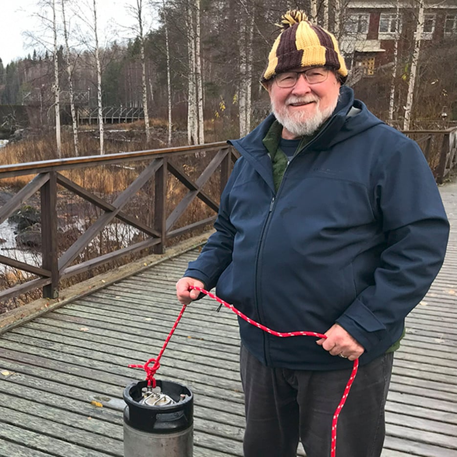 en glad herre står på en bro över en fors med ett rep i handen.