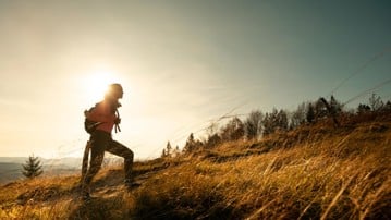 Hiker young woman with backpack rises to the mountain top on mountains landscape background