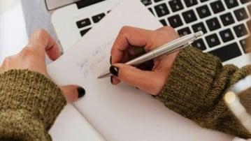 Hands writing on a piece of paper at a computer