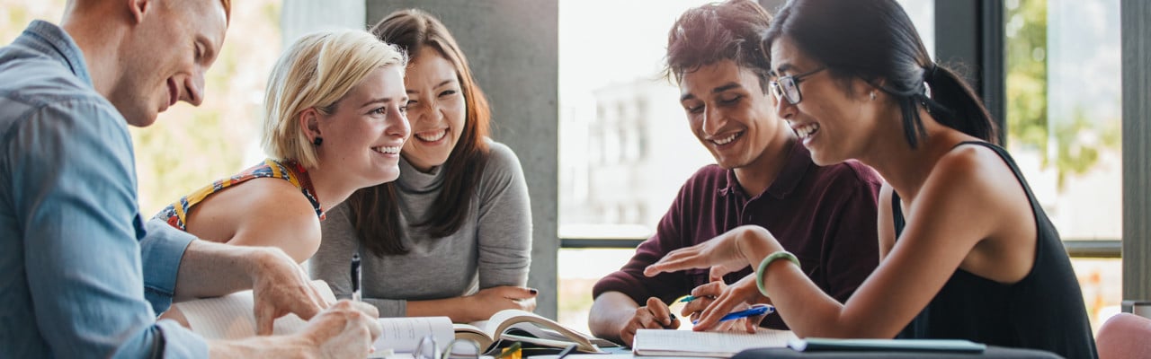 Happy young university students studying with books in library. Group of multiracial people in college library.