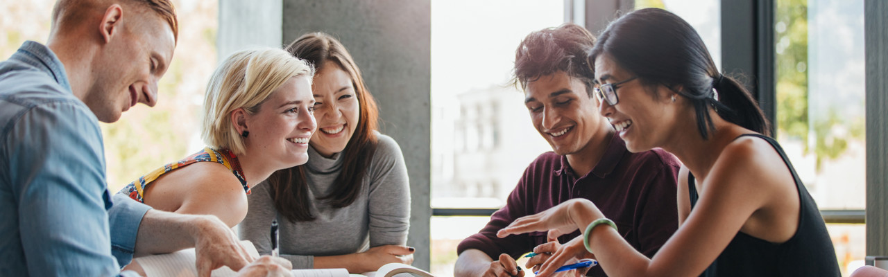 Happy young university students studying with books in library. Group of multiracial people in college library.