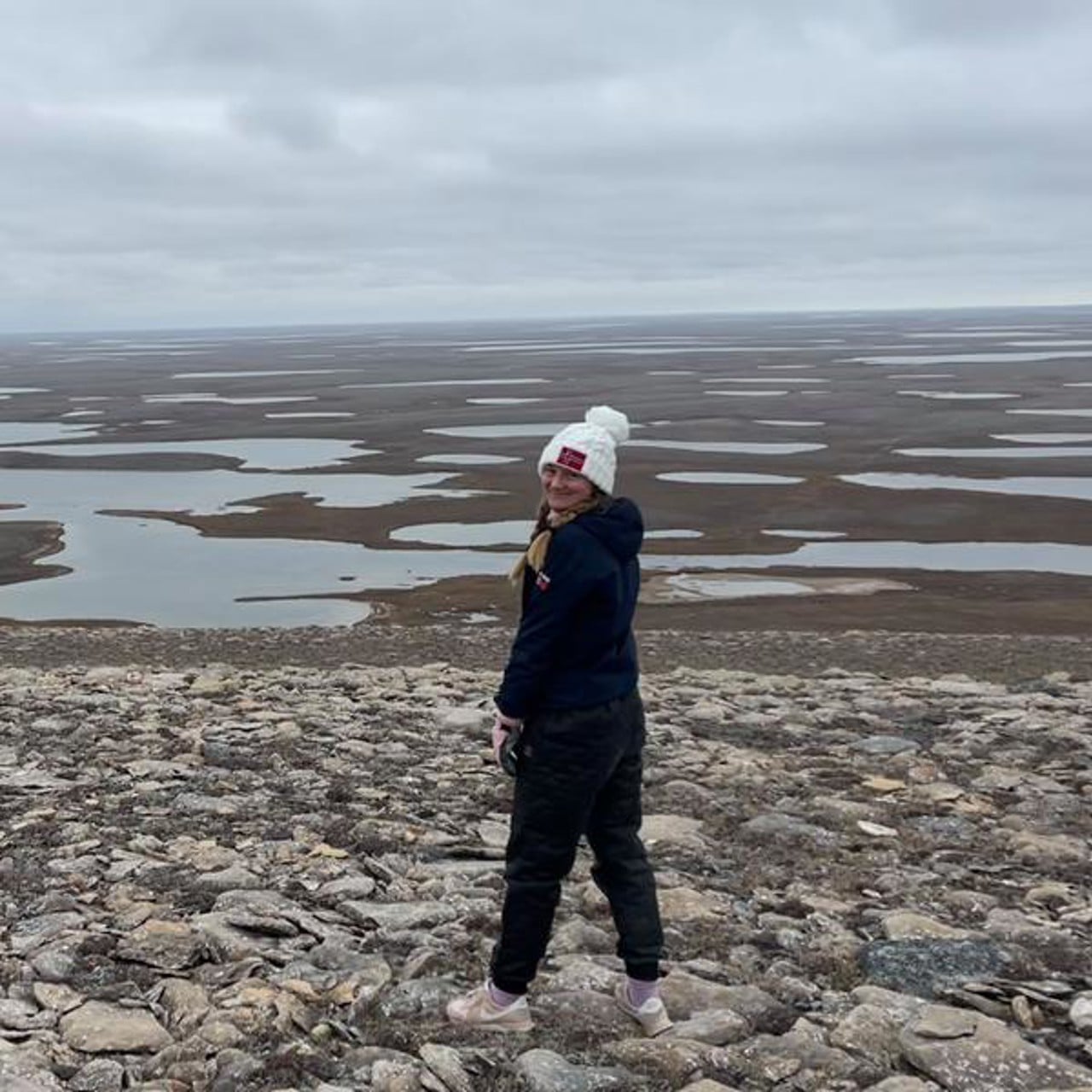 Lena Leimgruber Haraldsson står på en stenig strand med öppna slätter bakom sig.