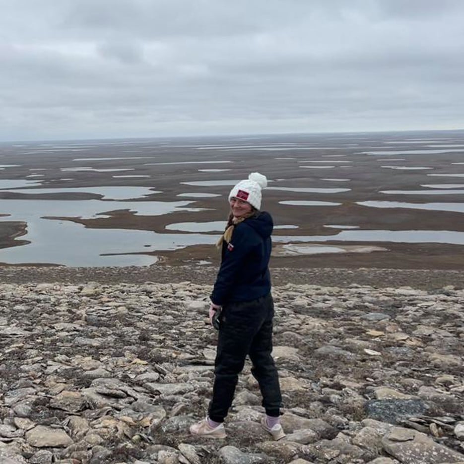 Lena Leimgruber Haraldsson står på en stenig strand med öppna slätter bakom sig.