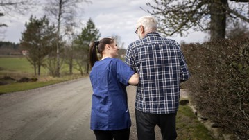 Kvinnlig hemtjänstpersonal hemma hos äldre man och tar promenad