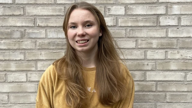 Porträttbild på Astrid Norstedt, beige tegelvägg i bakgrunden