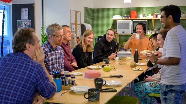 En grupp människor sitter runt ett träbord och delar tårta och pratar