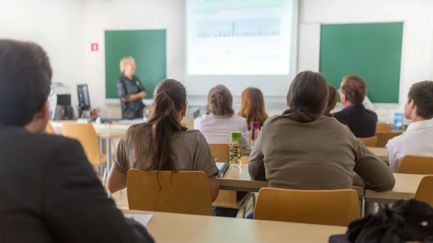 Föreläsningssal på universitet med studenter i förgrunden och en lärare vid tavlan.