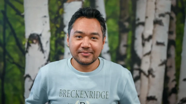 A portrait of a man in front of a wallpaper of birch trees