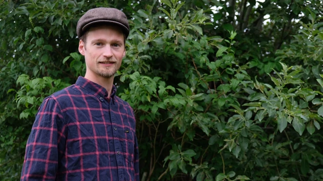 Man med hatt framför en stor buske