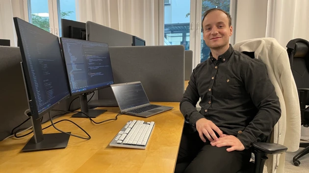 Bild på Jakub Jagiello sittande vid skrivbord omgiven av datorskärmar