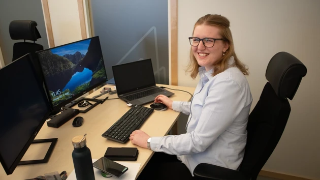 Bild på Linnea Stålstam sittande vid skrivbordet med flera datorskärmar framför sig