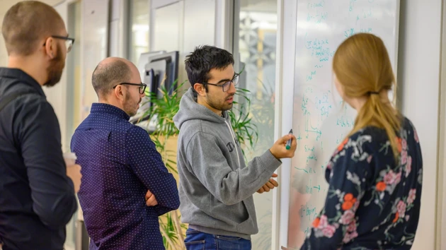 En grupp människor som står runt en whiteboardtavla