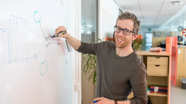 En man skriver på en whiteboardtavla i ett öppet kontorslandskap