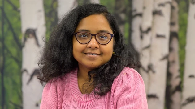 A woman in a pink sweater sitting in front of a birch tree background.