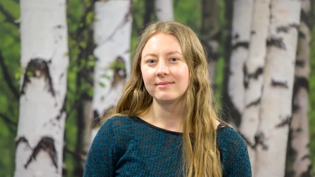 A woman standing in front of a painting of trees