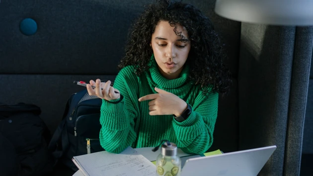 Studenten Sarah pluggar med dator och anteckningsblock.