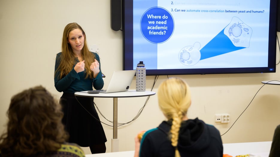 Verena Kohler stands in front of a screen and speaks to the Lunch Pitch audience seated in front of her.