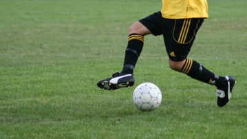 Detaljbild på person som dribblar med en fotboll på en gräsplan.
