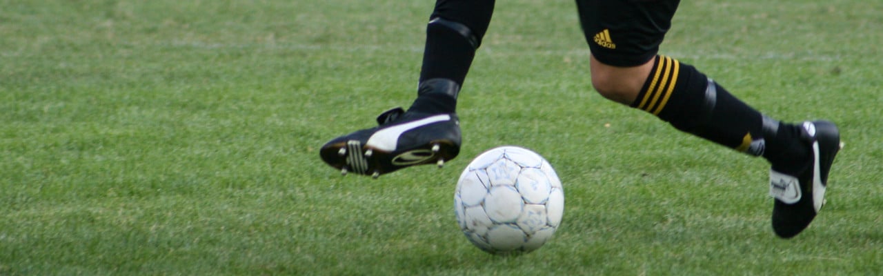 Detaljbild på person som dribblar med en fotboll på en gräsplan.
