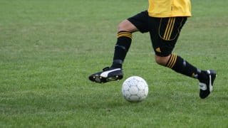 Detaljbild på person som dribblar med en fotboll på en gräsplan.
