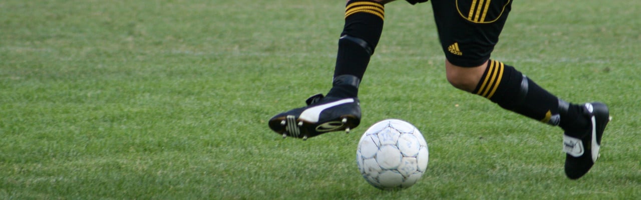Detaljbild på person som dribblar med en fotboll på en gräsplan.