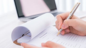 Hand med penna som ska kryssa i svar i en enkät. Bilden ska illustrera enkäter, mätningar, utvärdering.