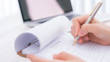 Hand med penna som ska kryssa i svar i en enkät. Bilden ska illustrera enkäter, mätningar, utvärdering.