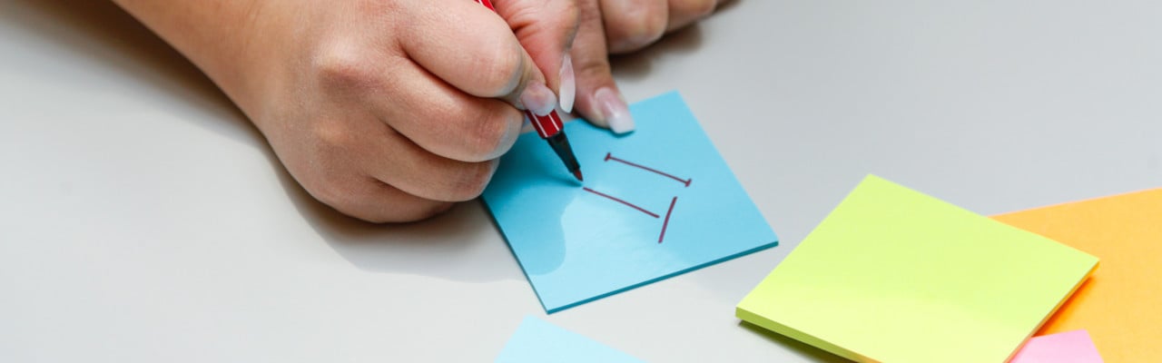 Hand som skriver IT på en post-it-lapp.