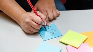Hand som skriver IT på en post-it-lapp.