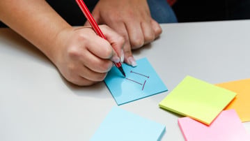 Hand som skriver IT på en post-it-lapp.
