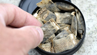 Hand som plockar upp en påse snus ur en snusdosa.