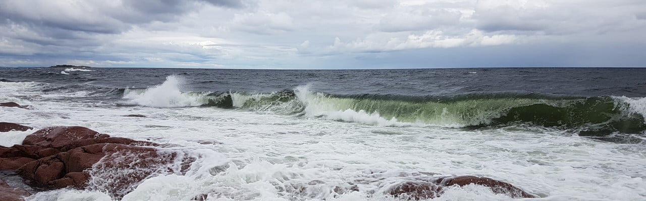 vågor slår mot röda klippor och en dramatisk himmel
