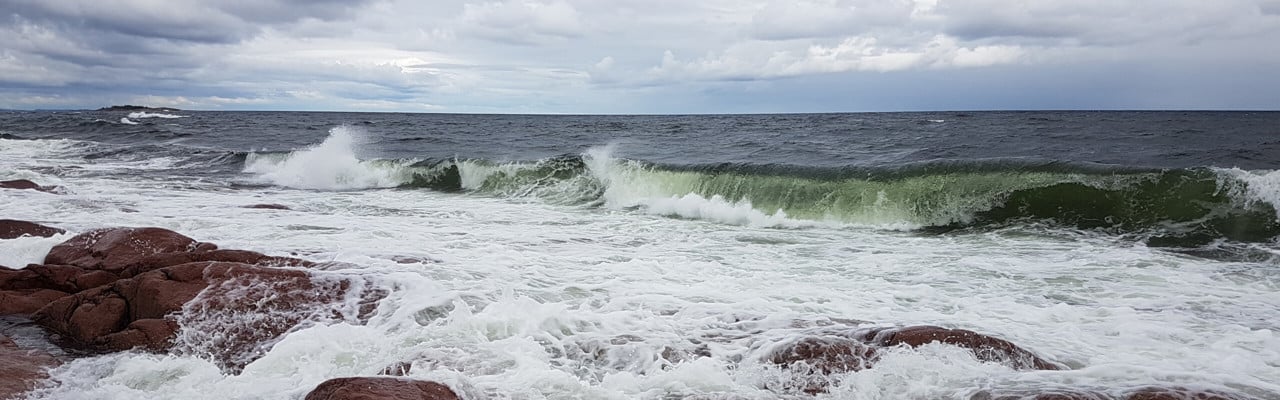vågor slår mot röda klippor och en dramatisk himmel